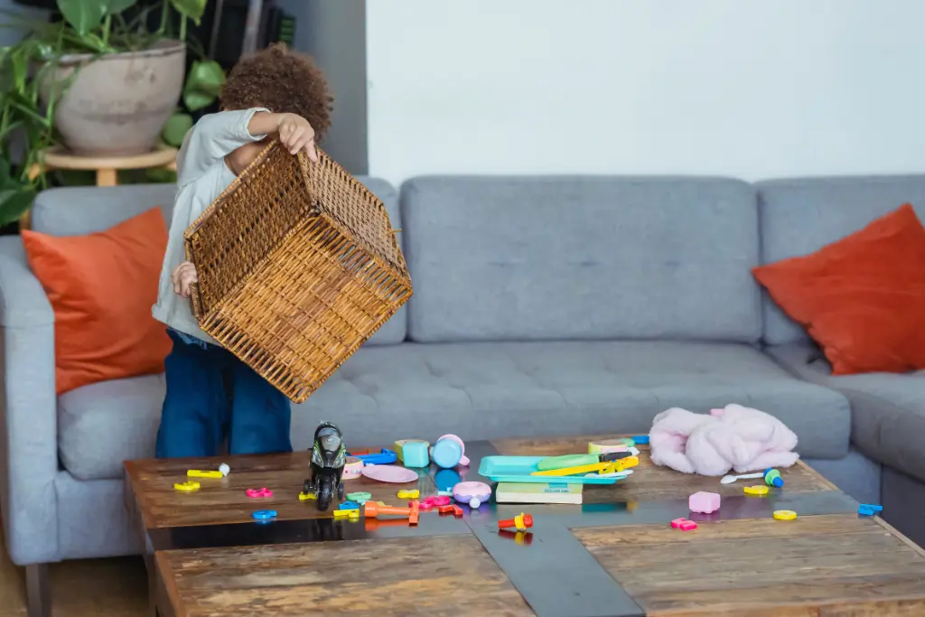 Jeune enfant renversant un panier de rangement de jouets sur une table basse