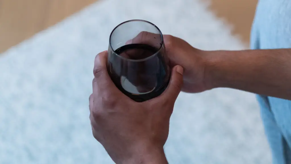 Personne tenant un verre de vin rouge au dessus d'un tapis blanc : que faire s'il est taché